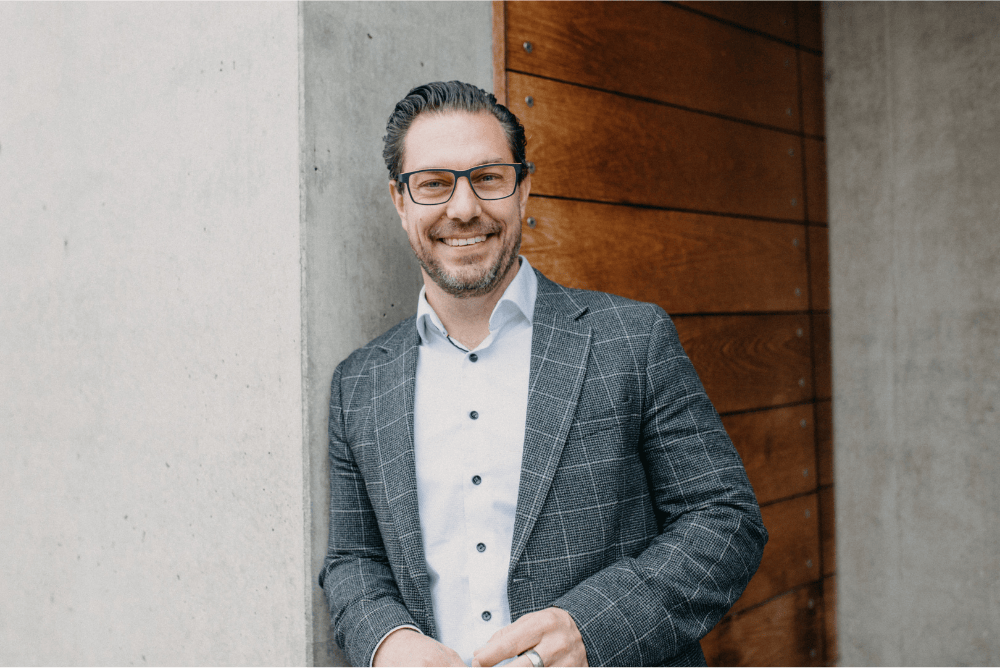 Business Coach Freiburg - Patrik Schönberger im Halbporträt vor einer Holztür – mit Sakko und freundlichem Blick, modernes und natürliches Porträtfoto